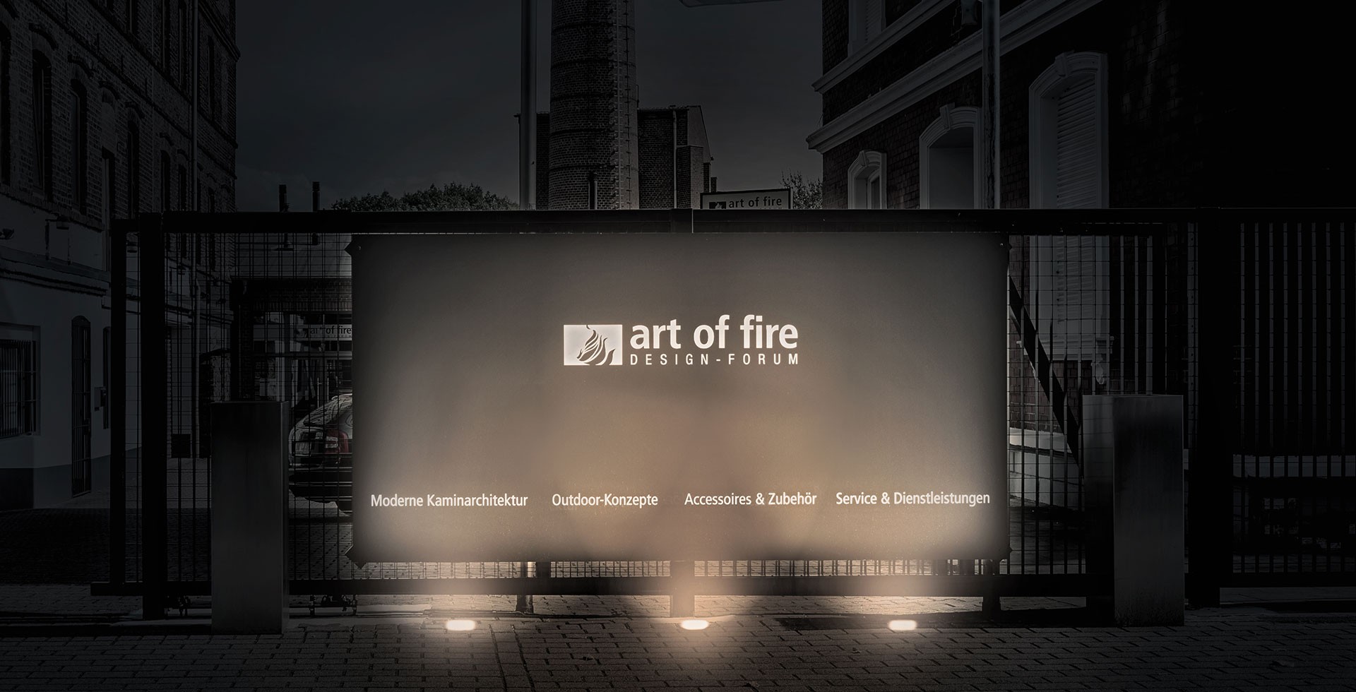 Zu sehen ist das Werbebanner von art of fire. Es ist ein grauen Plakat auf dem "Moderne Kaminarchitektur", "Outdoor